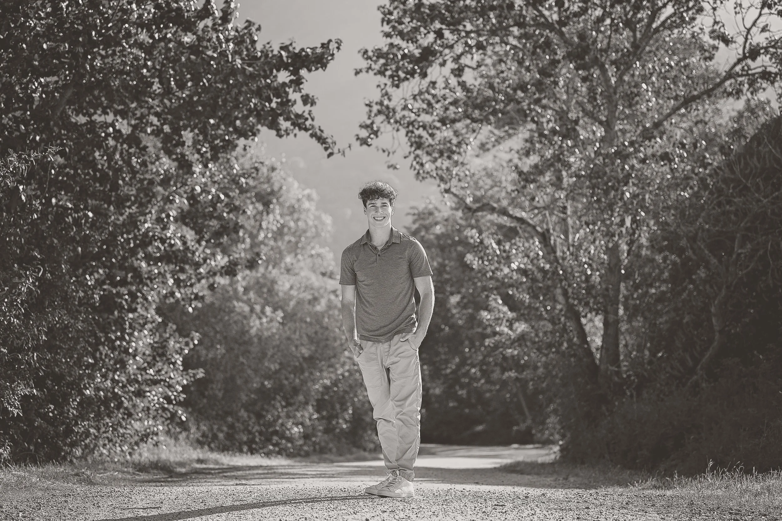 boy senior pictures on a path lined by trees in the evening sunshine