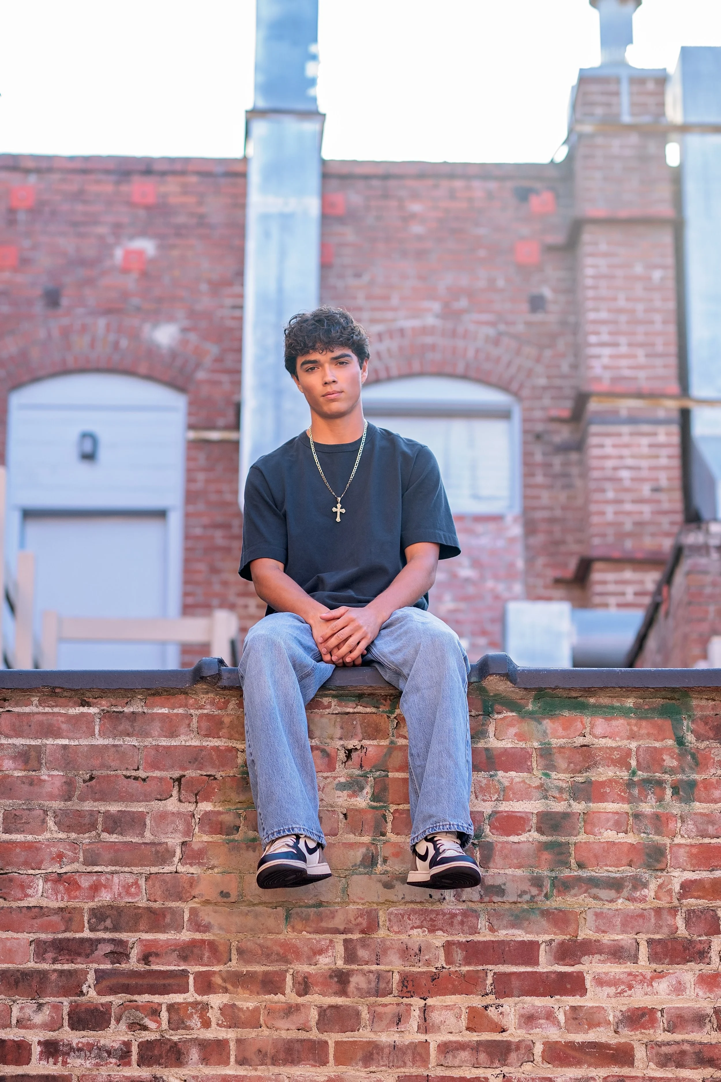 Cruz sitting on a brick ledge surrounded by historic architecture during his Downtown Salinas senior portrait session.