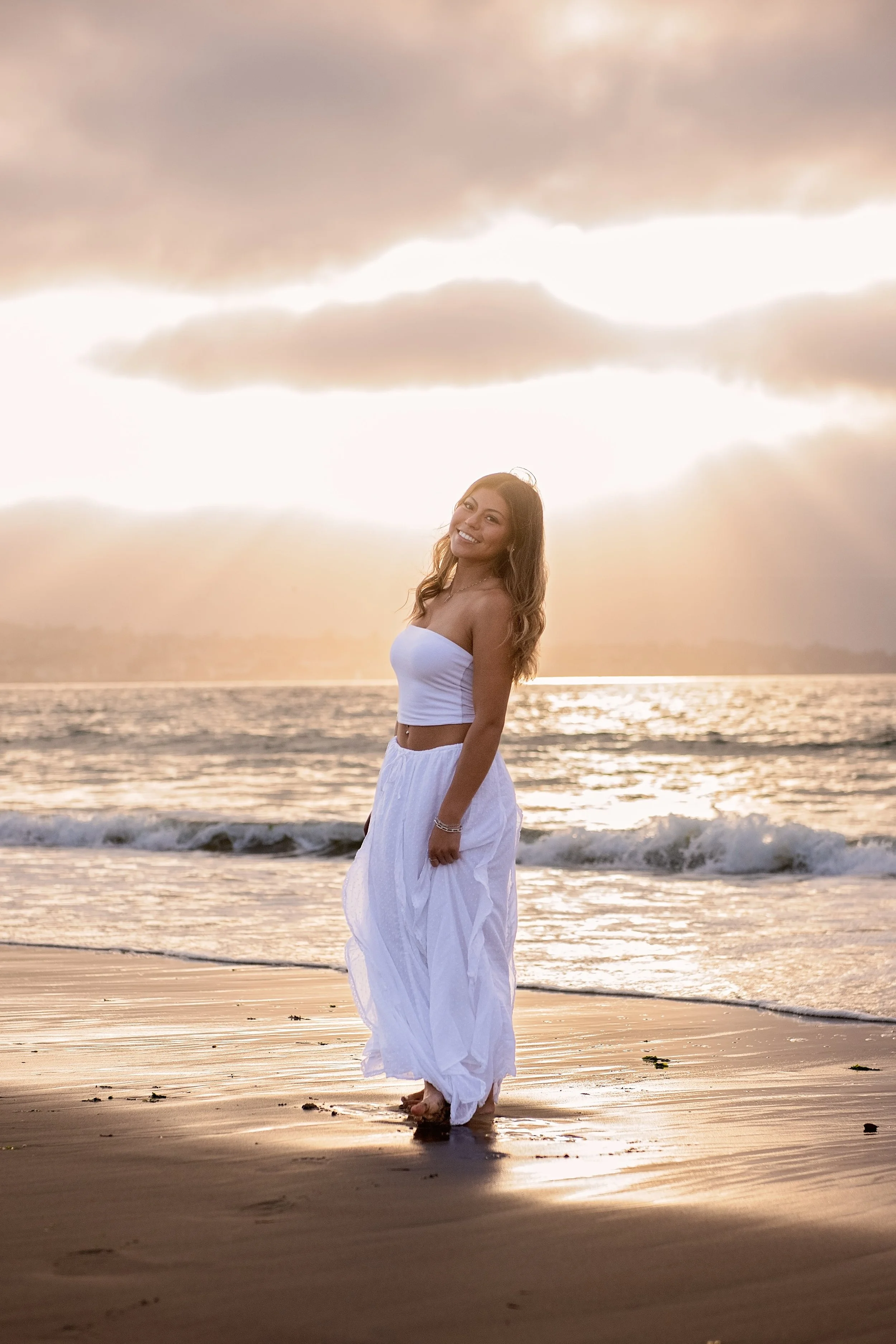 Golden hour senior portrait of Aubrey standing at the water’s edge at Del Monte Beach in Monterey