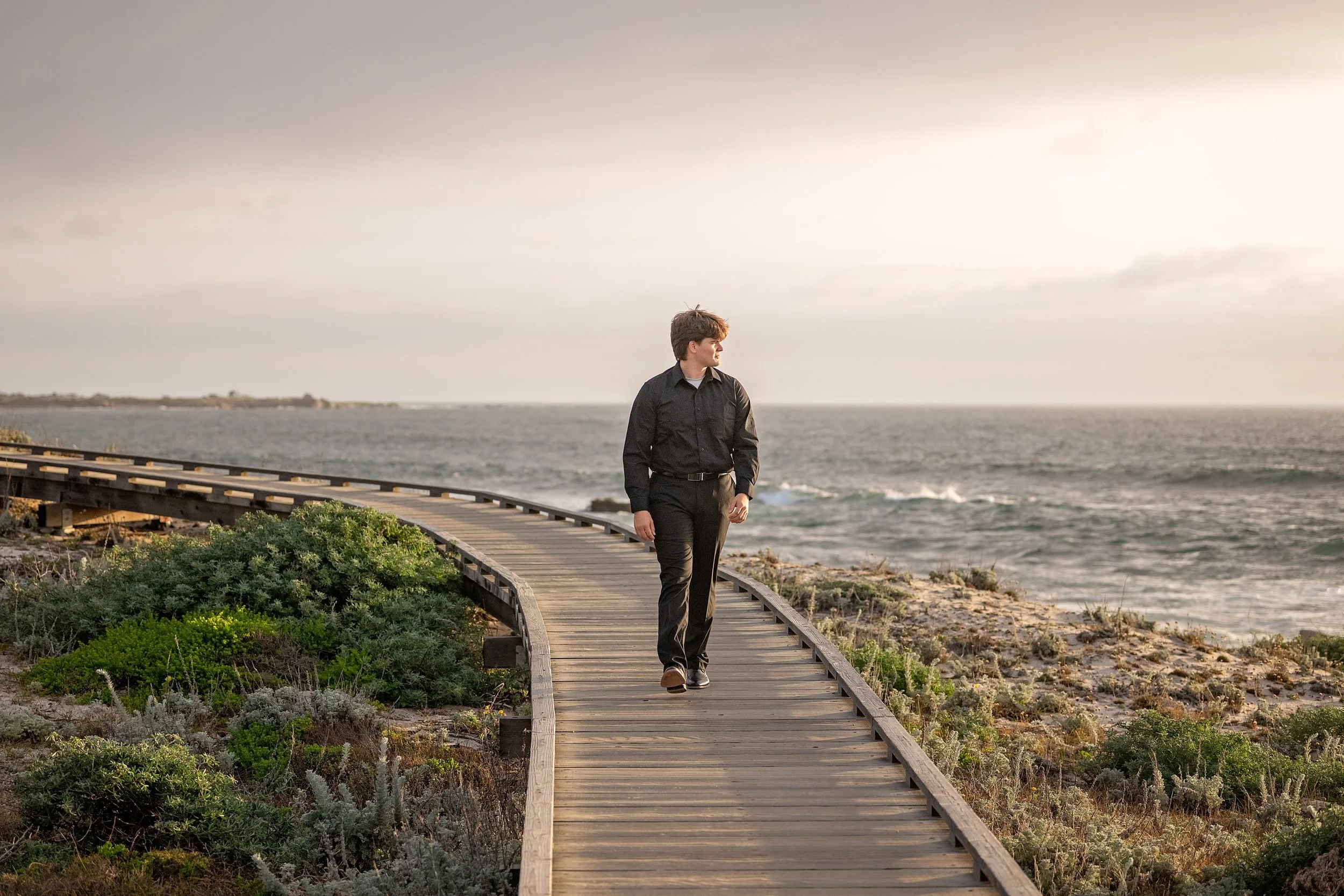 Gianni walking beside the Pacific Ocean on the boardwalk at Asilomar State Beach during golden hour.