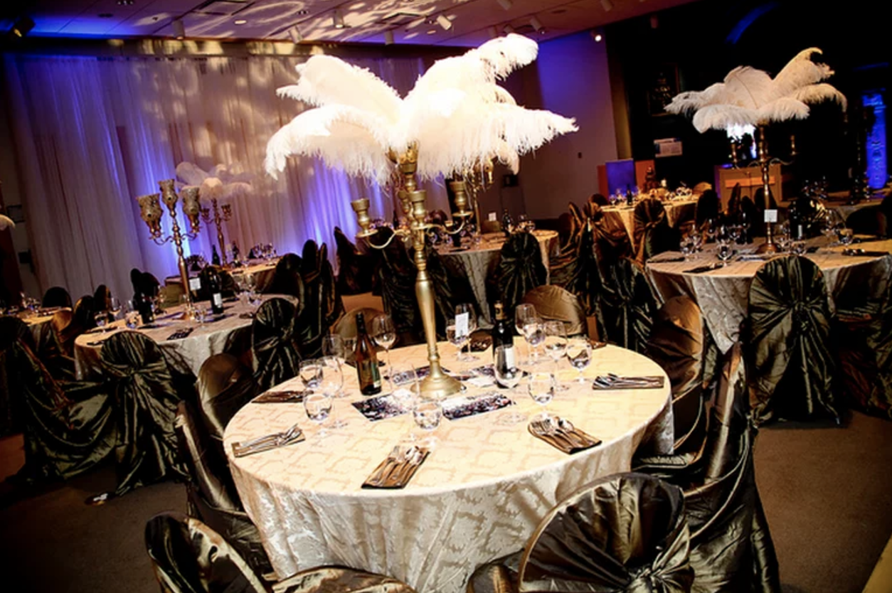 The dining hall had cream and gold tablecloths, dark henna green wrap chair covers, gold candelabras with ostrich feathers, paisley print gobo lighting on the focal wall and purple uplighting throughout the room. 