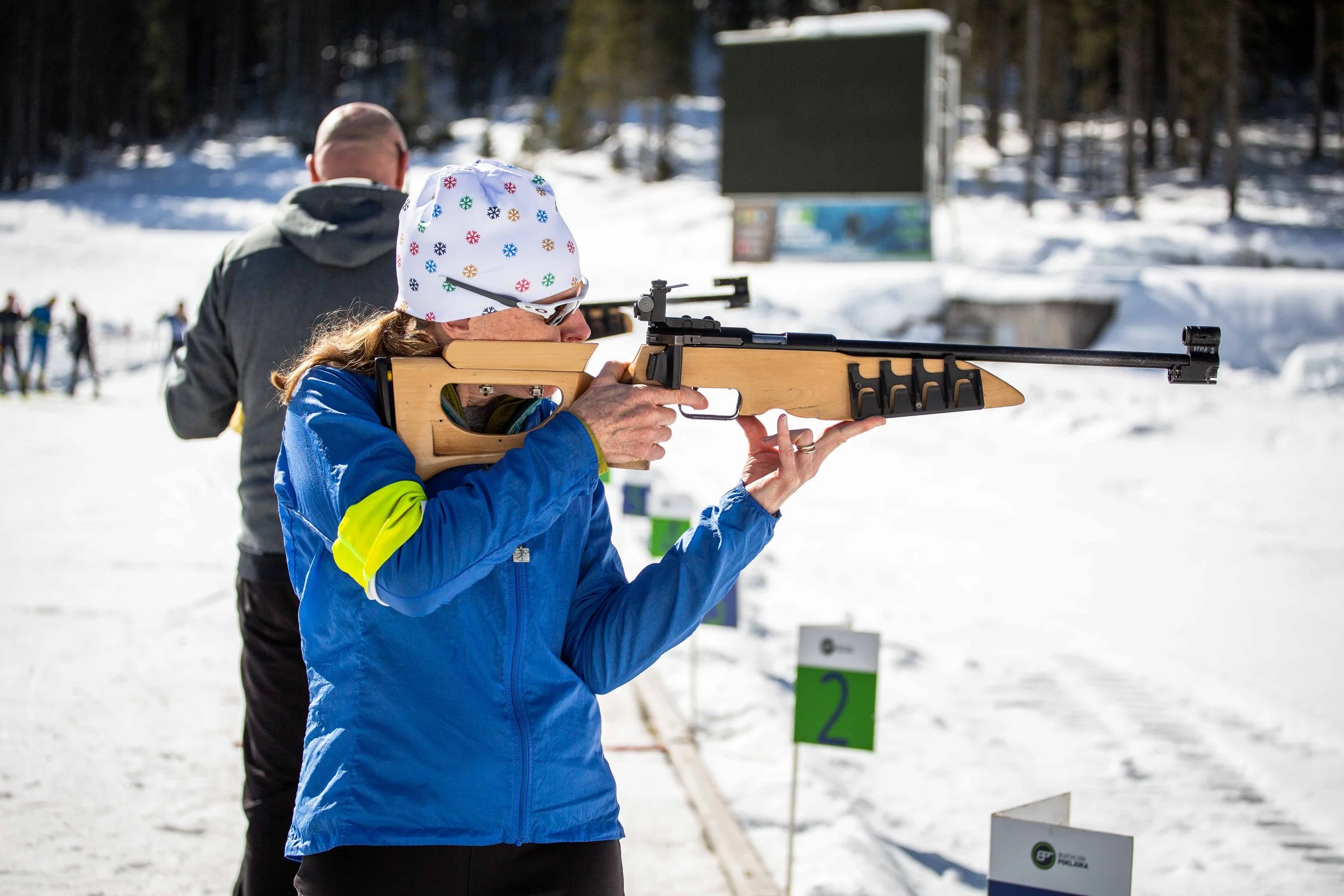 A female athlete stands with her rifle raised, taking aim