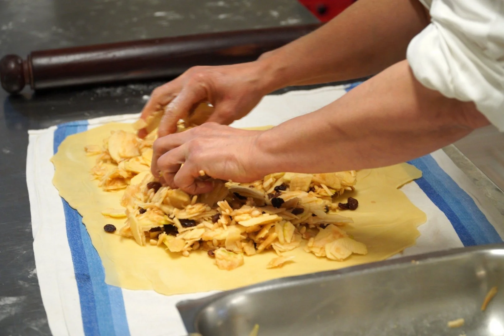 Hands filling thin pastry dough with apples, raisins, and pine nuts to make traditional Austrian apple strudel