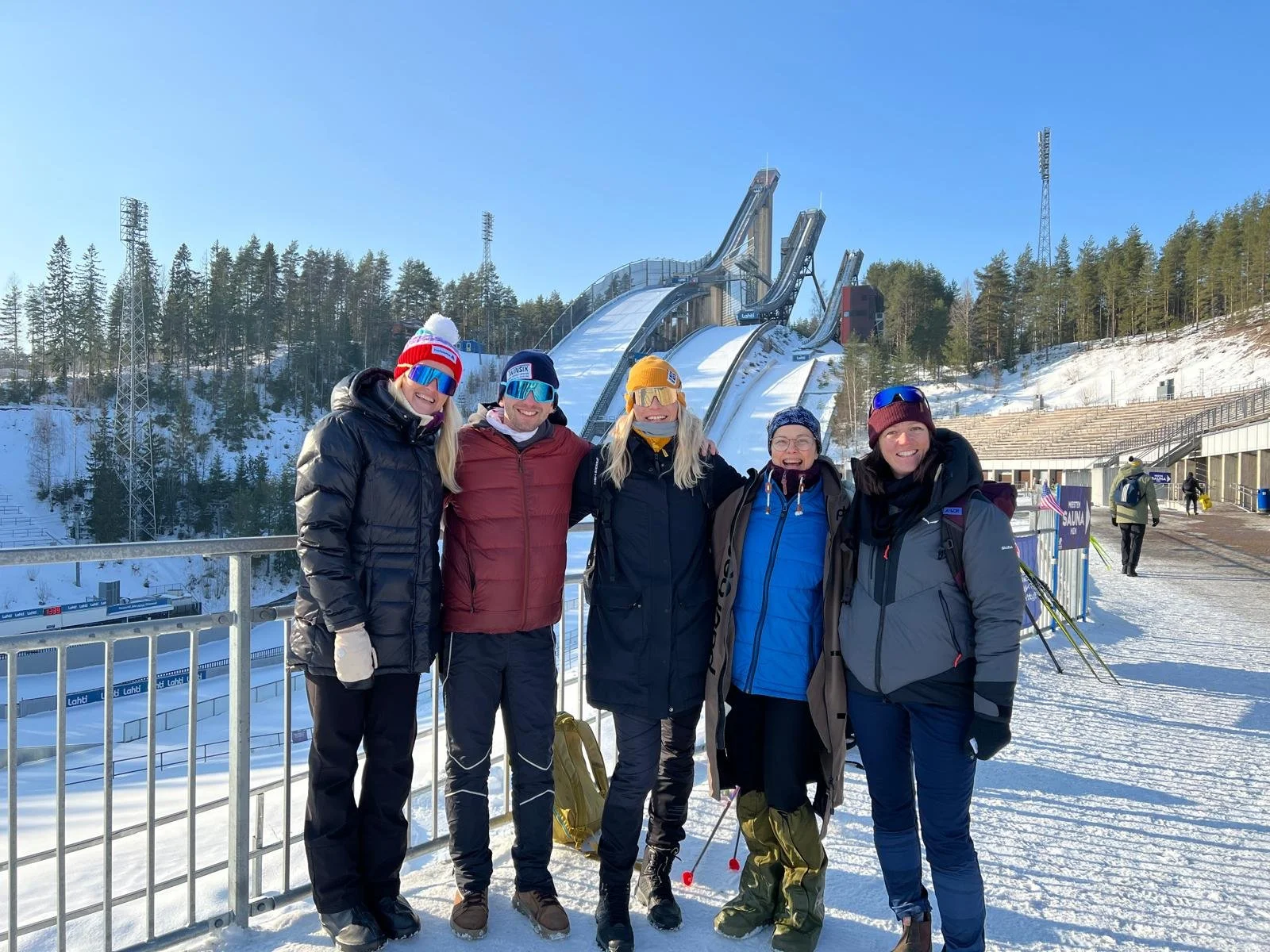 Skiers taking a cultural break to visit the iconic Lahti Ski Jump tower with their travel companions during a winter trip to Finland.