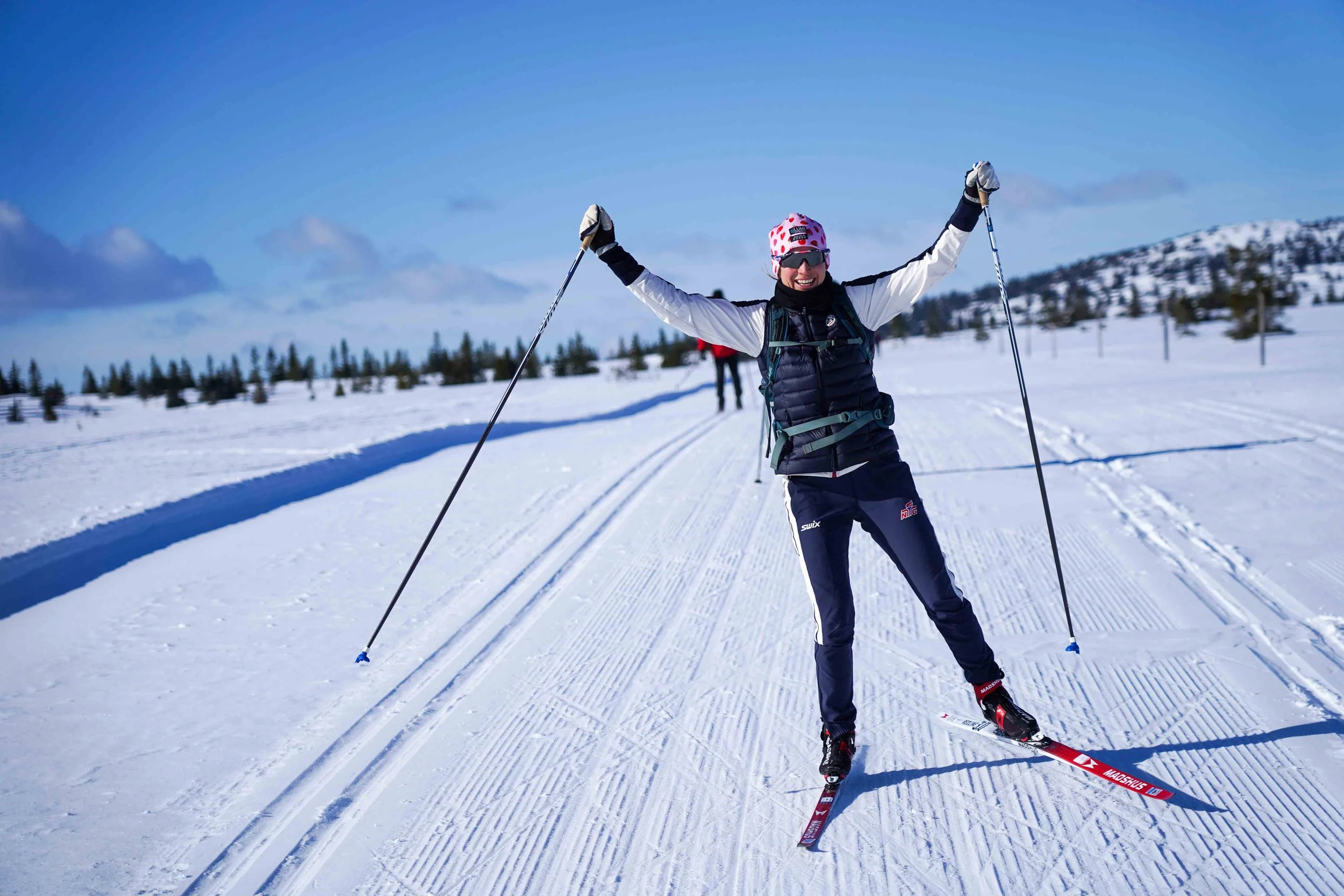 Smiling woman cross-country skiing in a snowy Norwegian landscape.