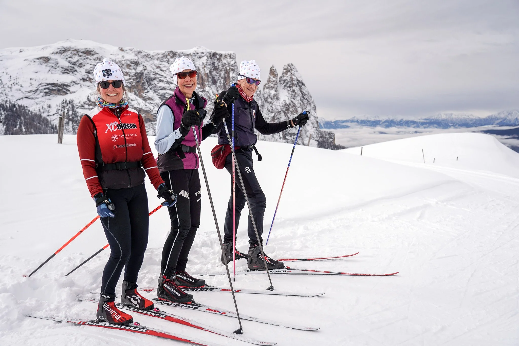 Three cross-country skiers gliding across the snow-covered Seiser Alm plateau with a panoramic mountain backdrop of the Schlern