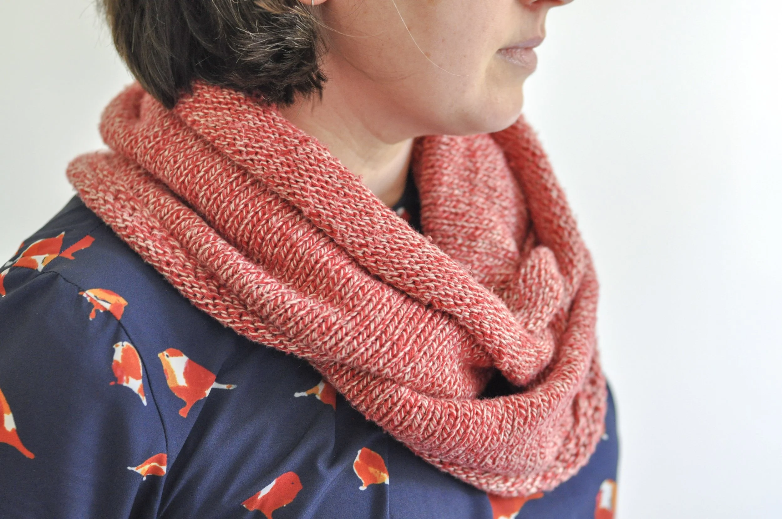 A woman waring a long cowl in red variegated yarn