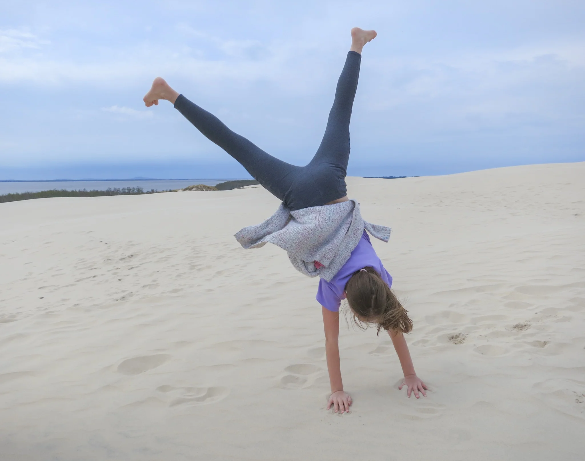 A girl does a cartwheel on the Łackca Sand Dune In Słowiński National Park