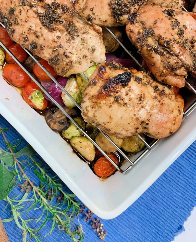 Balsamic marinated chicken thighs on a wire rack over roasted Brussels sprouts, mushrooms, and grape tomatoes in a baking dish