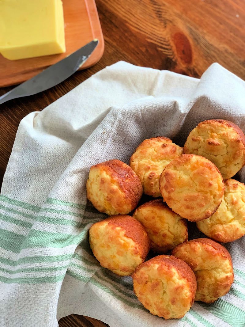 Golden almond flour cheddar biscuits fresh from a muffin tin, soft and buttery with visible cheddar throughout