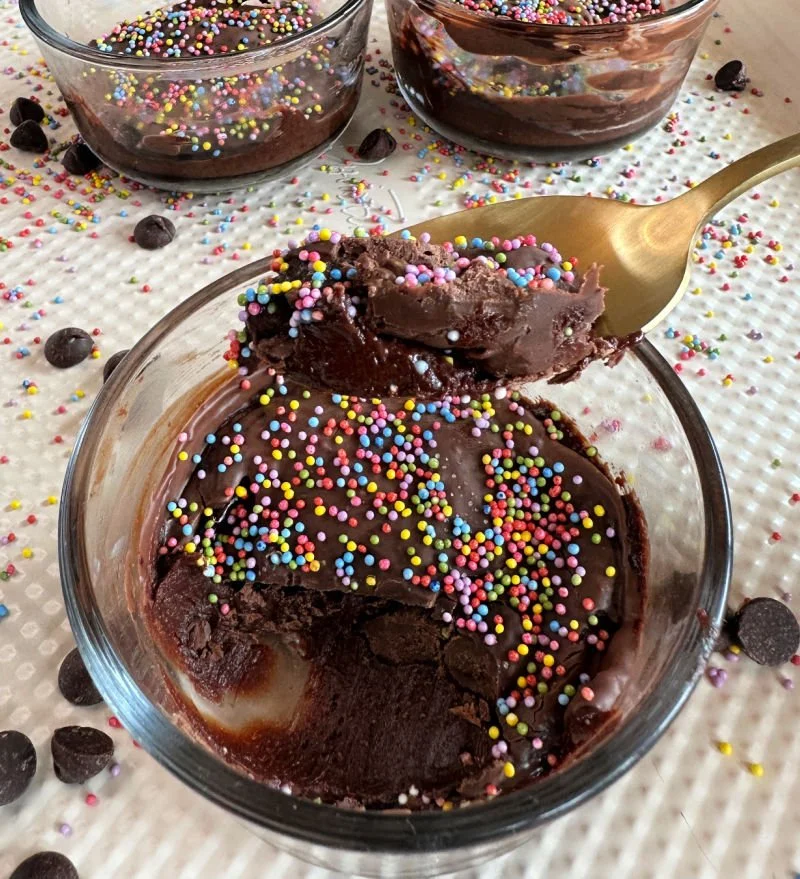 Cosmic brownie protein dessert cups in glass bowls with Lily's chocolate frosting and dye-free rainbow sprinkles on top