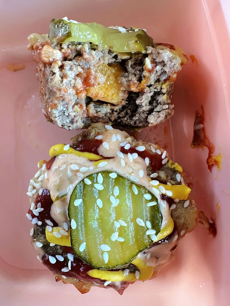 High protein cheeseburger muffins with a cheesy center in a muffin tin next to sugar-free burger sauce and raw vegetables