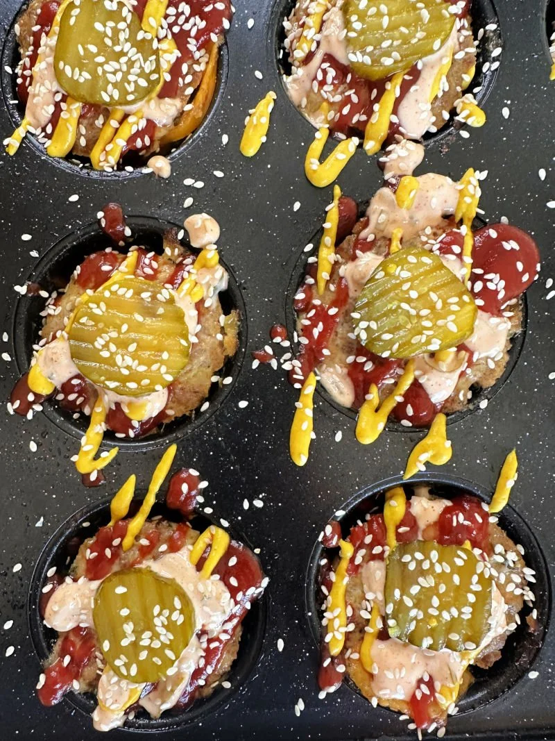 High protein cheeseburger muffins with a cheesy center in a muffin tin next to sugar-free burger sauce and raw vegetables