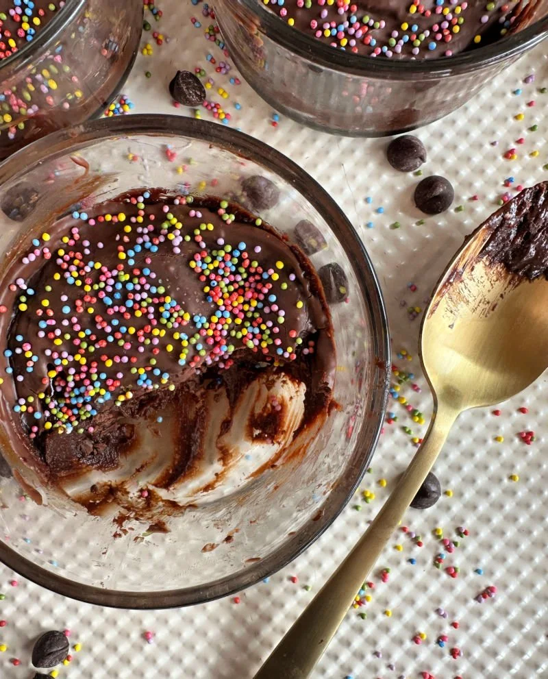 Cosmic brownie protein dessert cups in glass bowls with Lily's chocolate frosting and dye-free rainbow sprinkles on top
