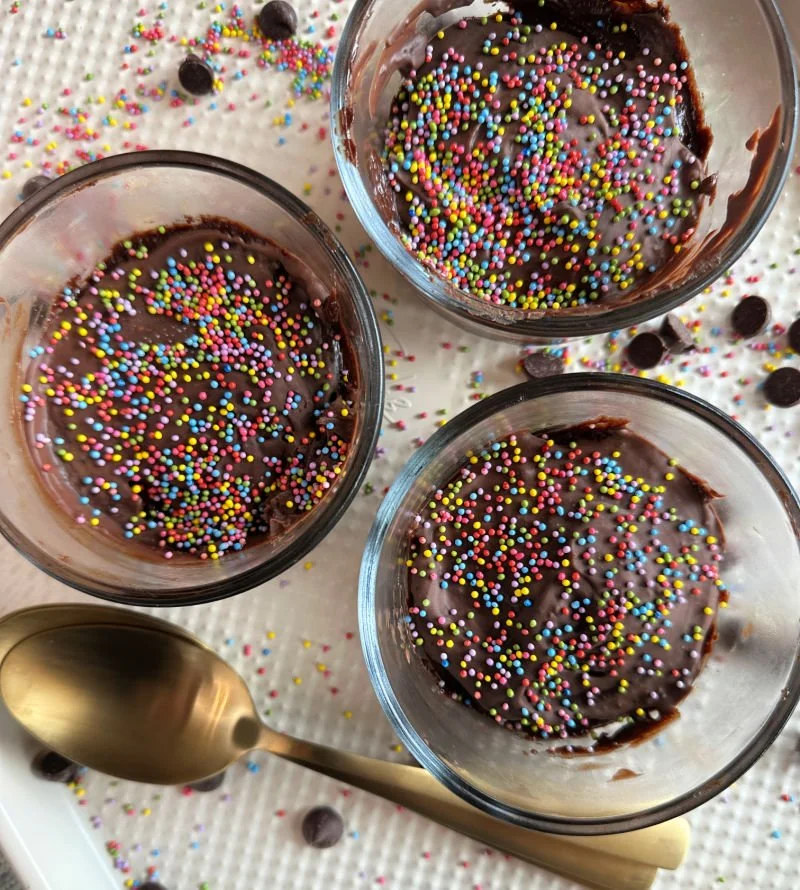 Cosmic brownie protein dessert cups in glass bowls with Lily's chocolate frosting and dye-free rainbow sprinkles on top