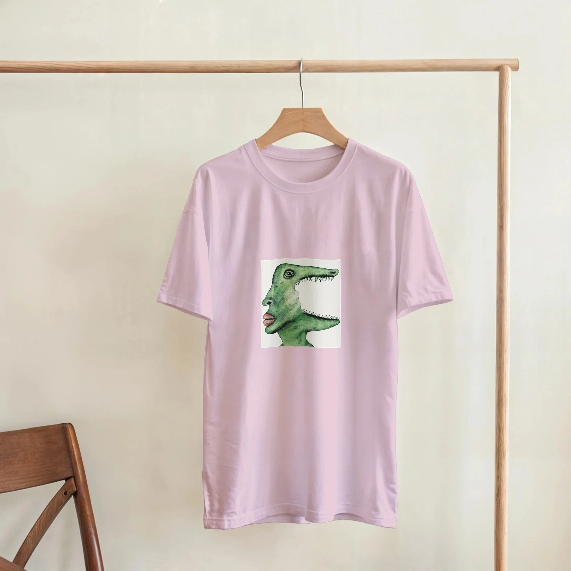 Unisex light pink t-shirt featuring a green surrealist crocodile art print by Roi Pajursky, modeled in various lifestyle settings.