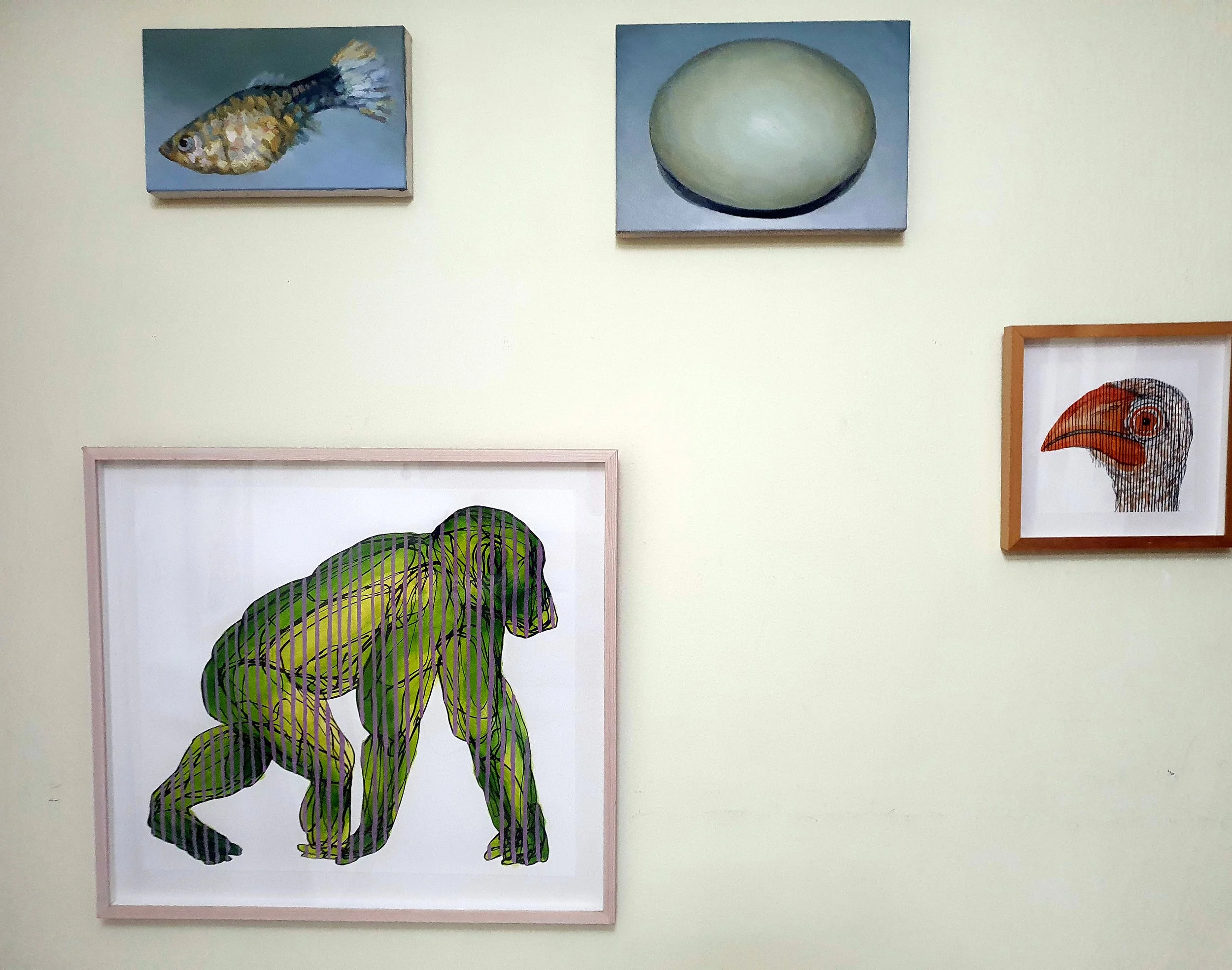 A curated gallery wall featuring traditional oil paintings of a fish and egg alongside modern graphic biological art.