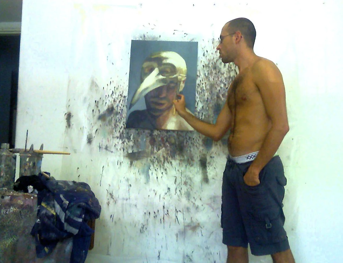 Artist Roi Pajursky working on a large-scale oil painting of a masked figure in his studio.