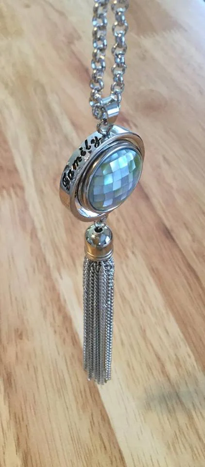 FAMILY" TASSEL NECKLACE $14.00 This long necklace if full of movement and interest. The word "Family" is visible on top of the outer ring, framing the snap which swivels slightly, and the tassel at the bottom gives the necklace even more interest. -20.5 inches including tassel -Includes 1 large, light blue, mosaic shell snap -Interchangeable with other large snaps