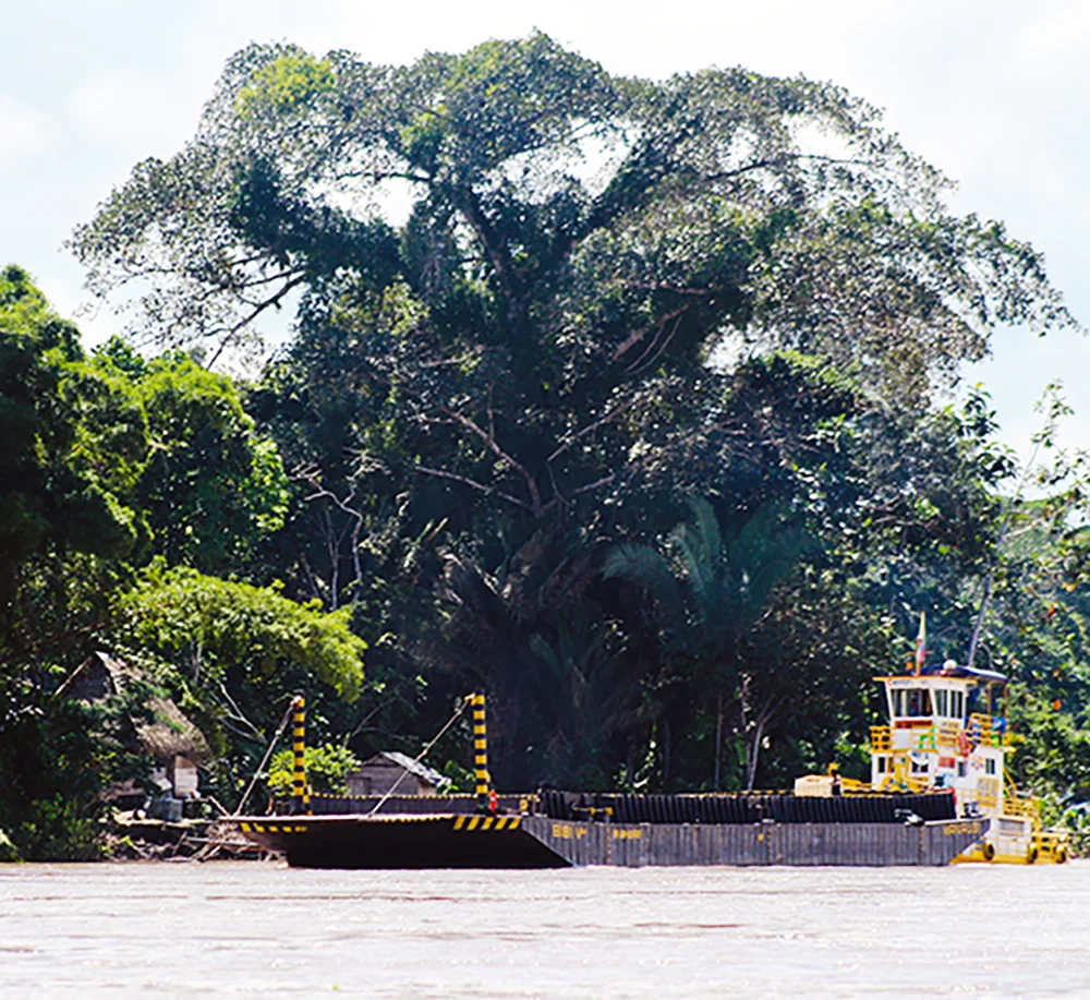 A tow boat pushes a barge past a village on the Napo river. Many indigenous young people grow up in the traditional way, but within sight of the 21st century. (Sierra Bilton)