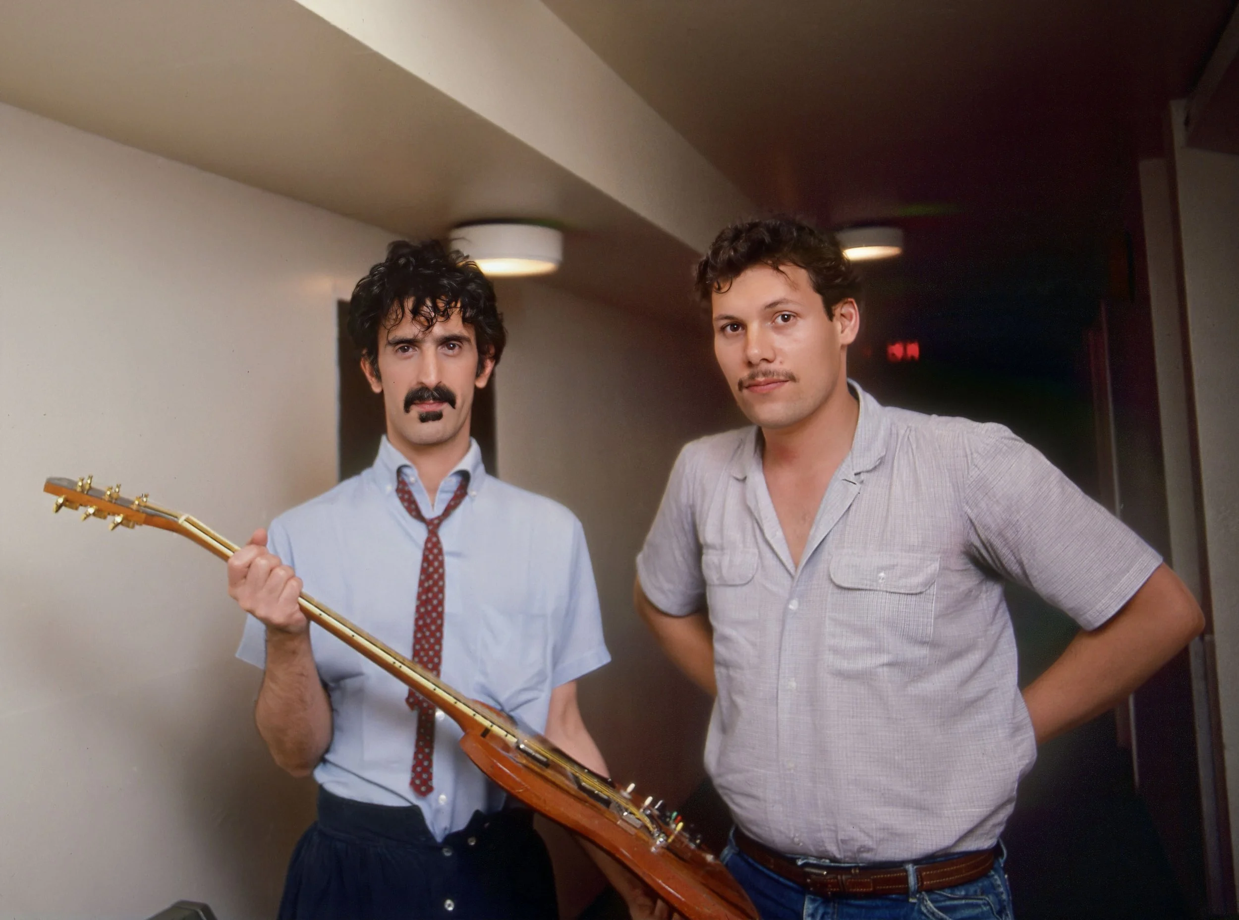 Frank Zappa and Bart Nagel standing indoors, one holding a guitar, both looking at the camera.