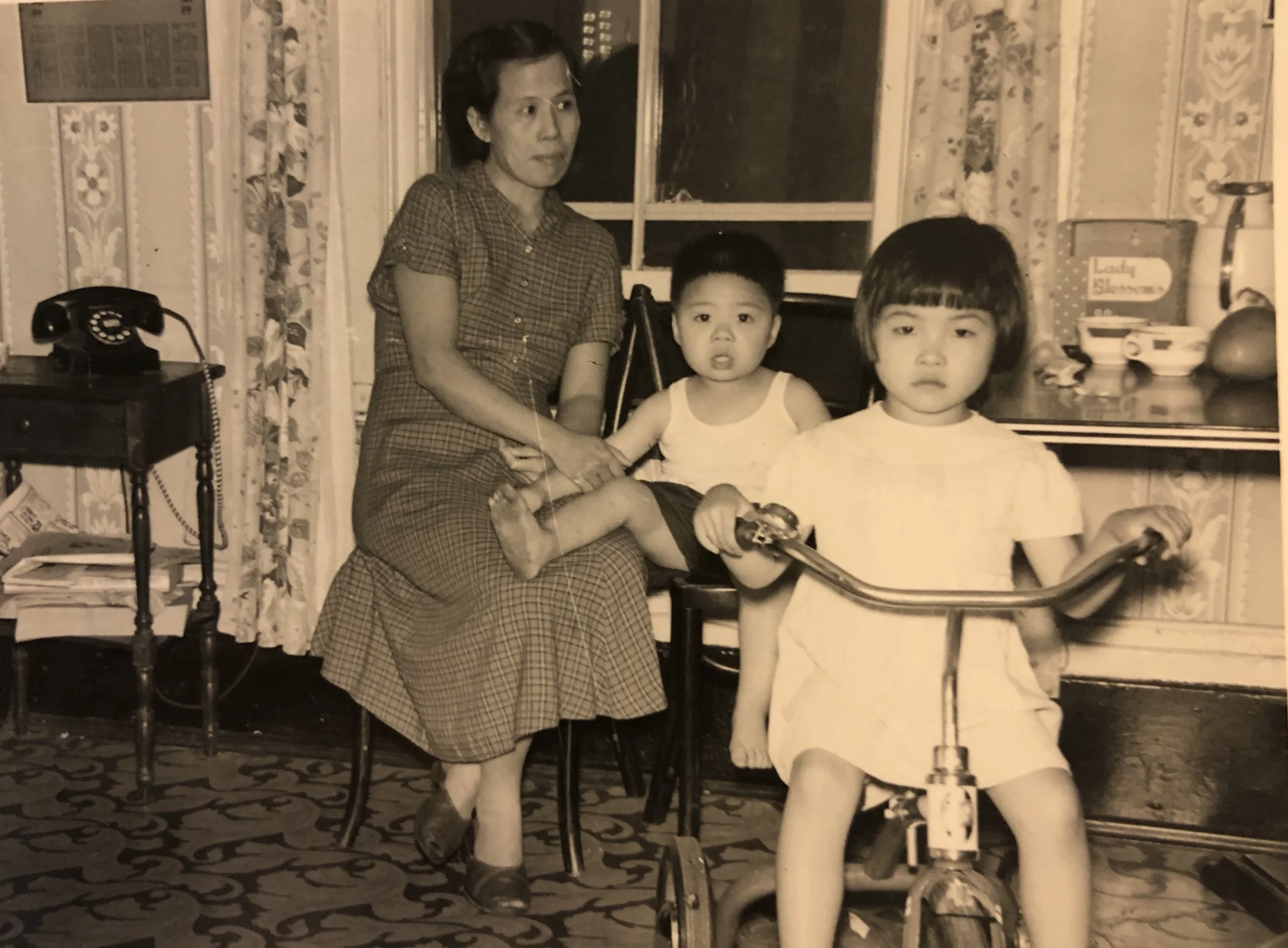 Cynthia on a tricycle with her cousin Albert and her mother May Soon Yee inside her home on the second floor of 116 Hudson Street, 1950’s