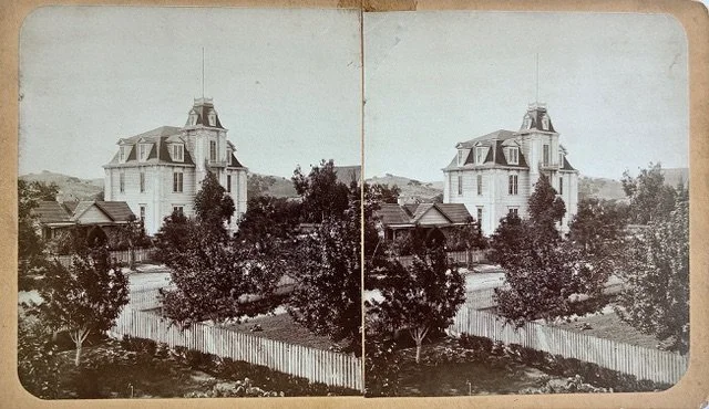 A stereographic image of an 19th century high school with a picket fence in the foreground.