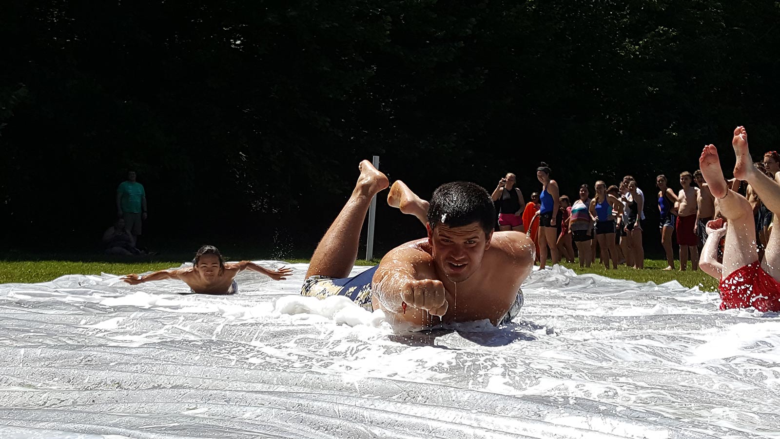 Teenager or camp counselor and young Asian boy sliding on their stomach on a homemade slip & slide - NaCoMe Camp & Conference Center