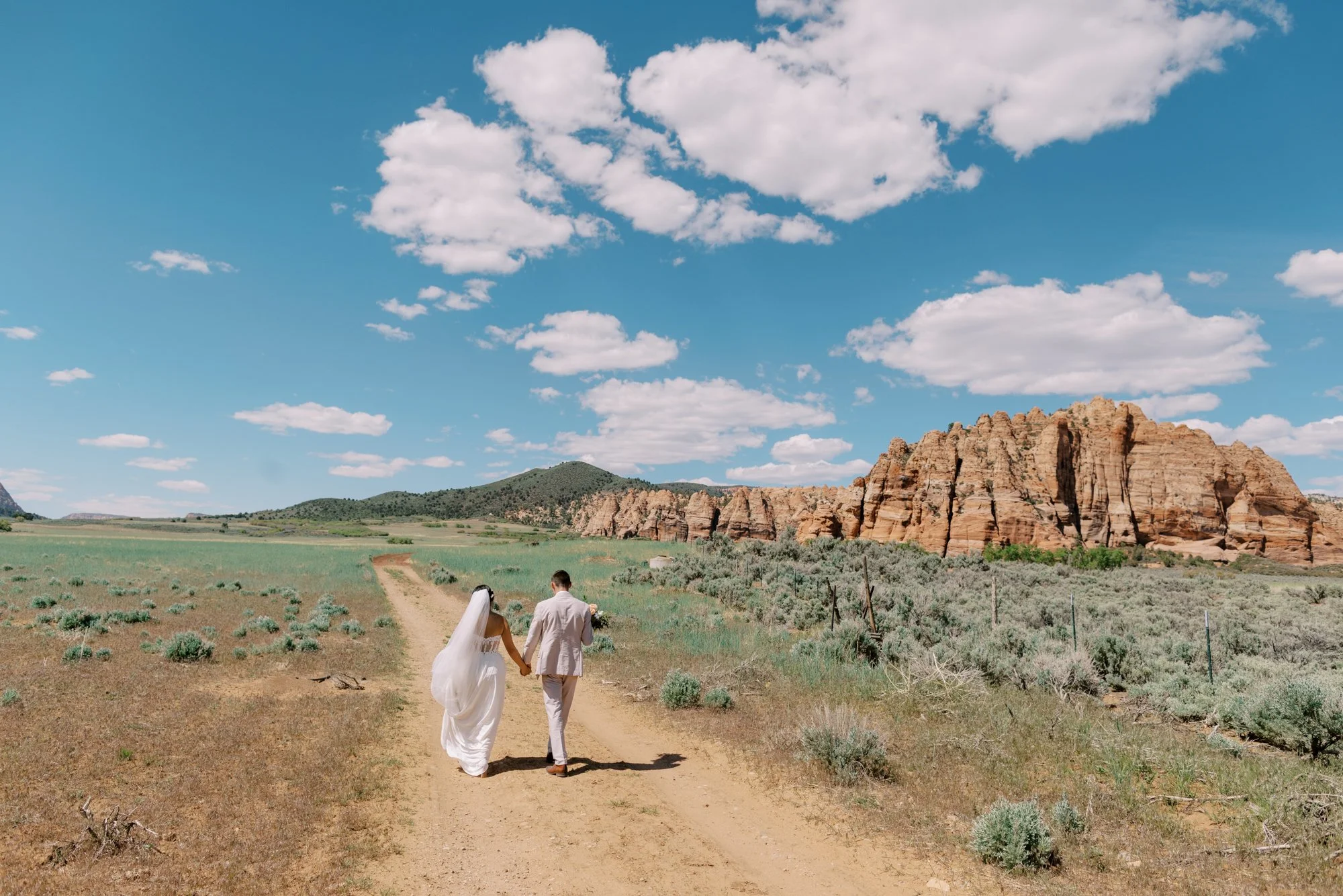 Zion National Park Wedding Photographer, Wedding at Autocamp Zion, Bride and Groom walking through a field at a wedding near Zion National Park, Autocamp wedding, Zion film photography