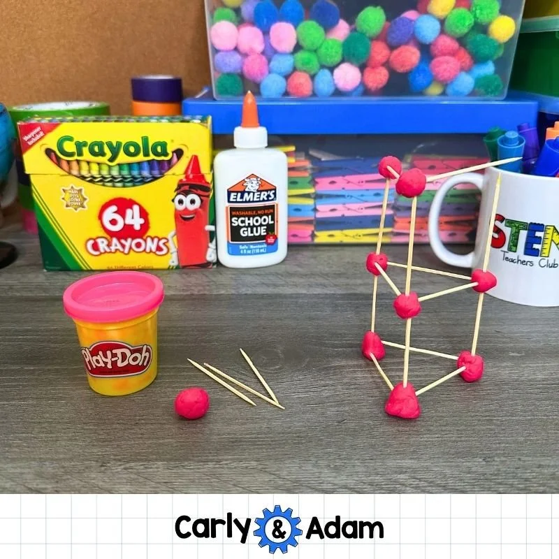 Close-up of a two-level toothpick tower with bright pink play dough joints. A Play-Doh container, a small ball of dough, and loose toothpicks sit to the left.