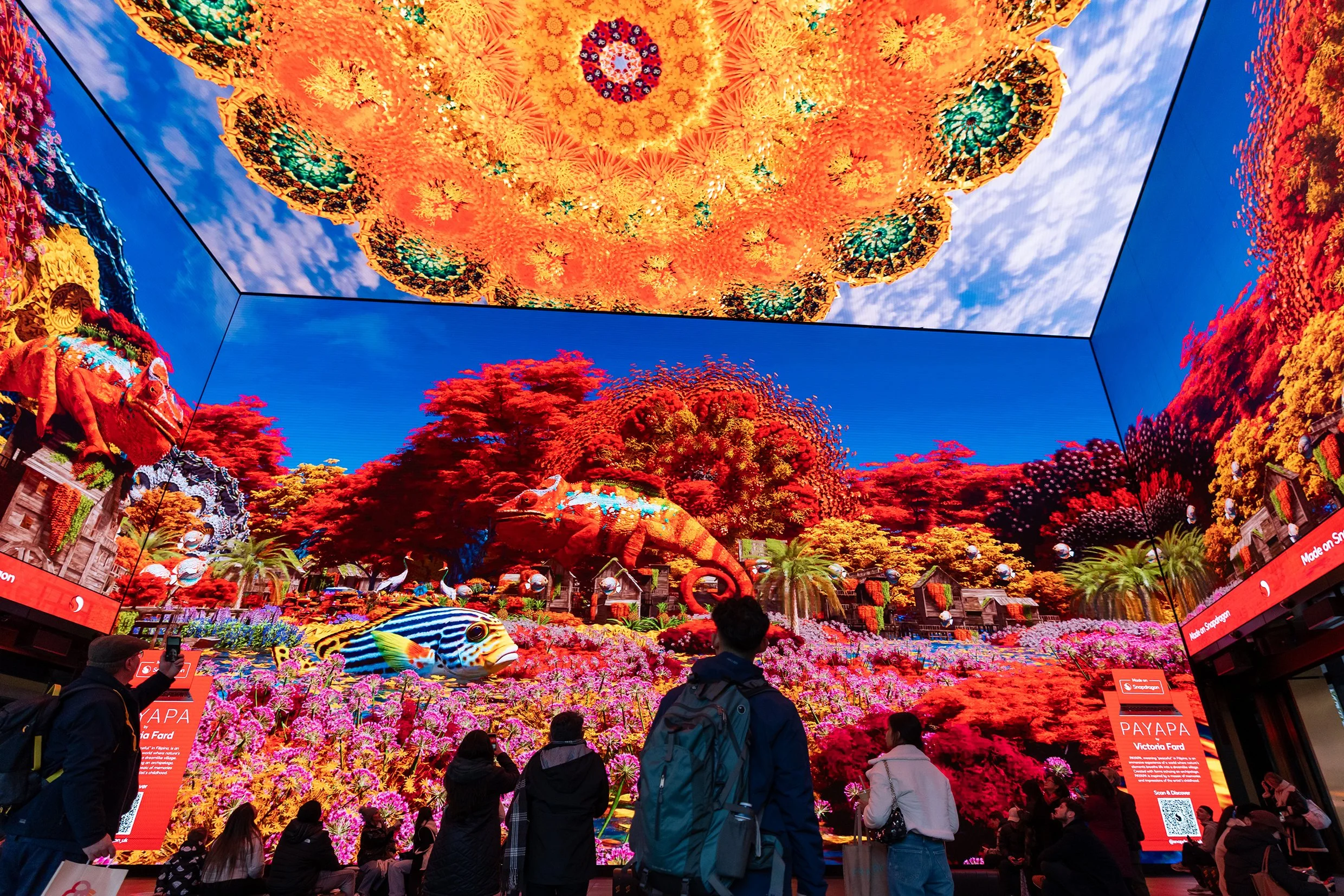 People observing digital screens depicting vibrant tropical landscape scenes with large colorful flowers, lush red and orange trees, and intricate cloud patterns.