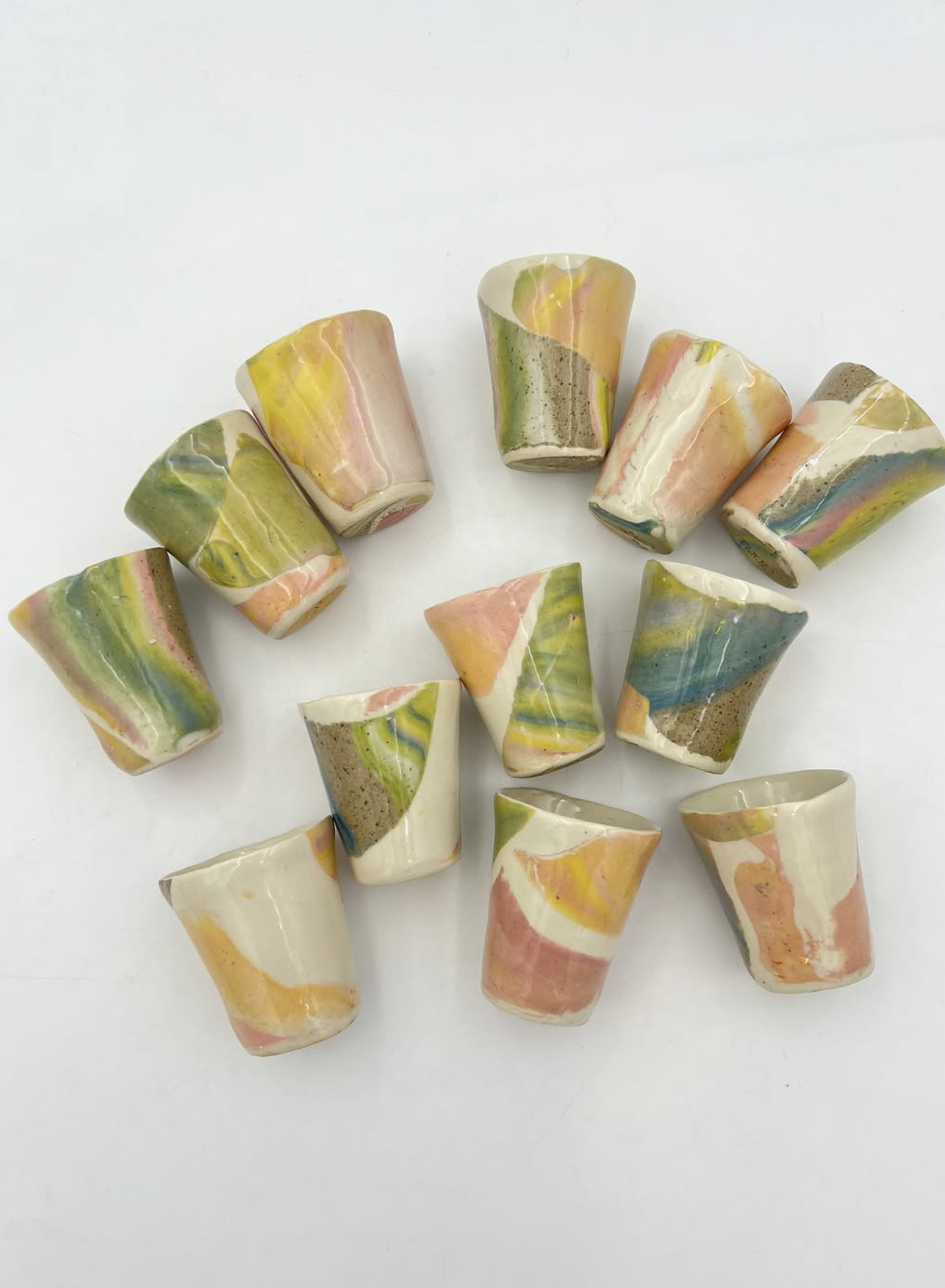Multiple handmade ceramic cups with marbled pastel colors arranged on a white surface.