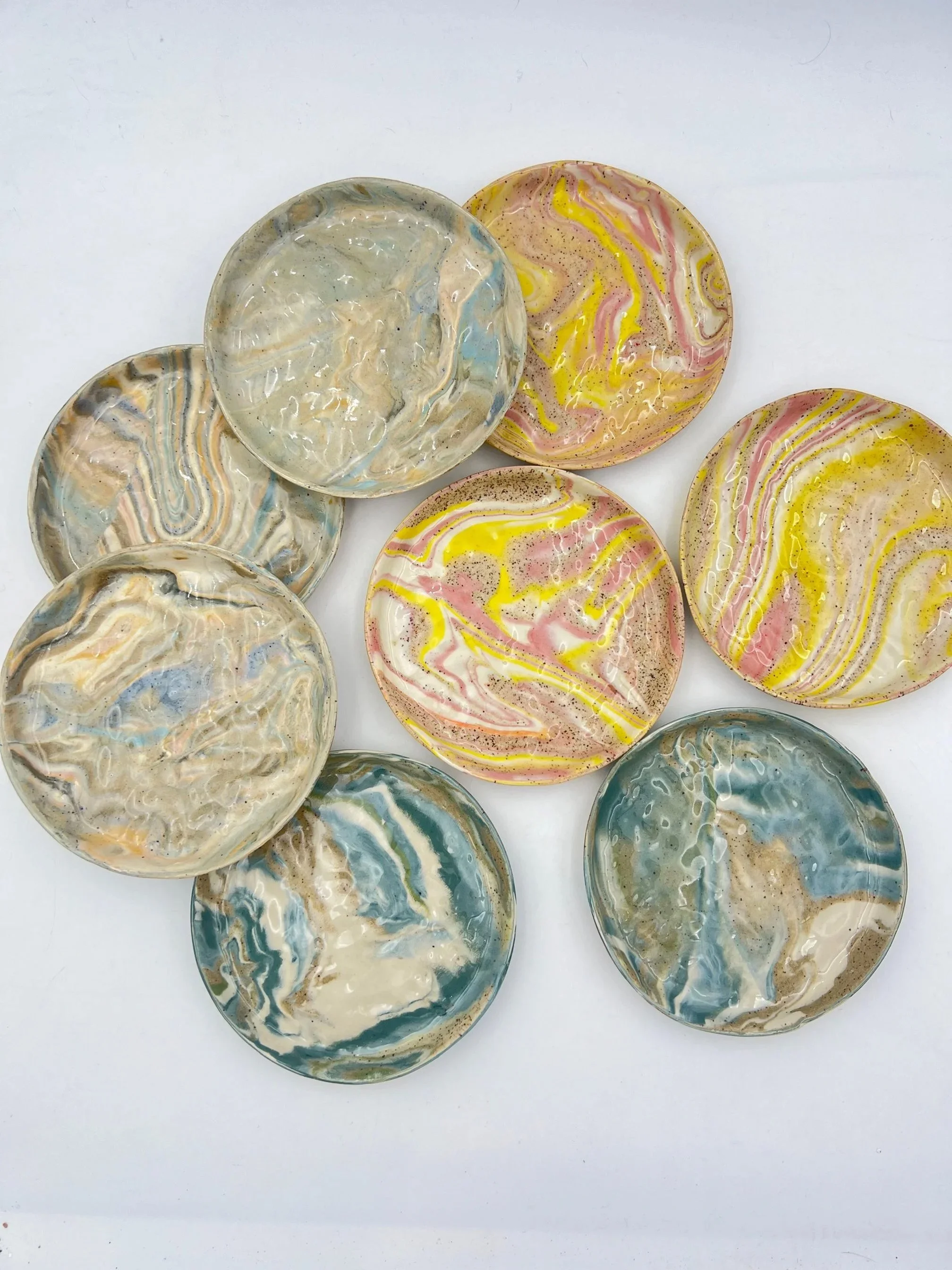 Multiple marbleized resin coasters with swirling patterns in blue, pink, yellow, and beige colors on a white background.