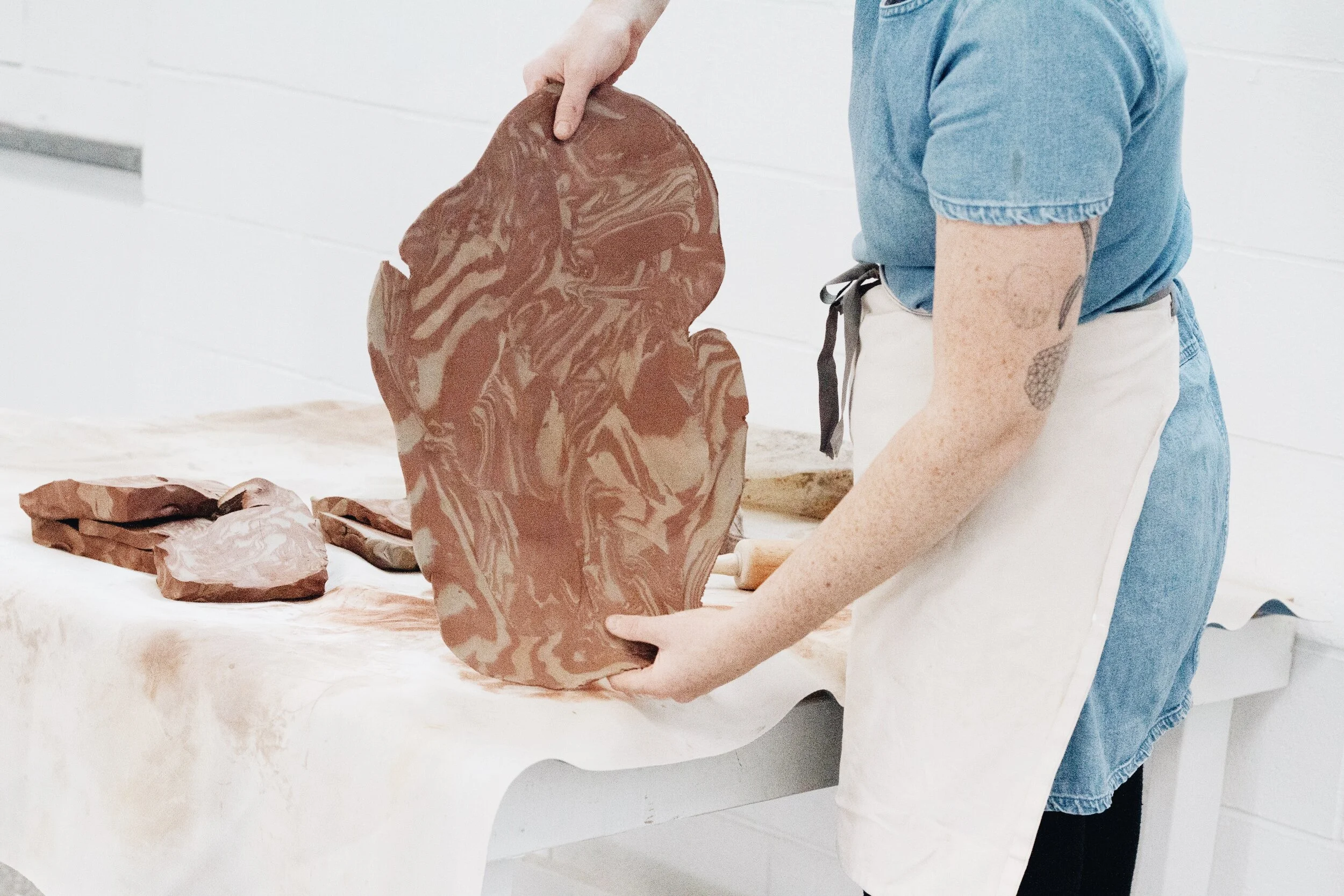 Person in a blue denim shirt and white apron arranging marbled brown and beige paper bags on a white table.