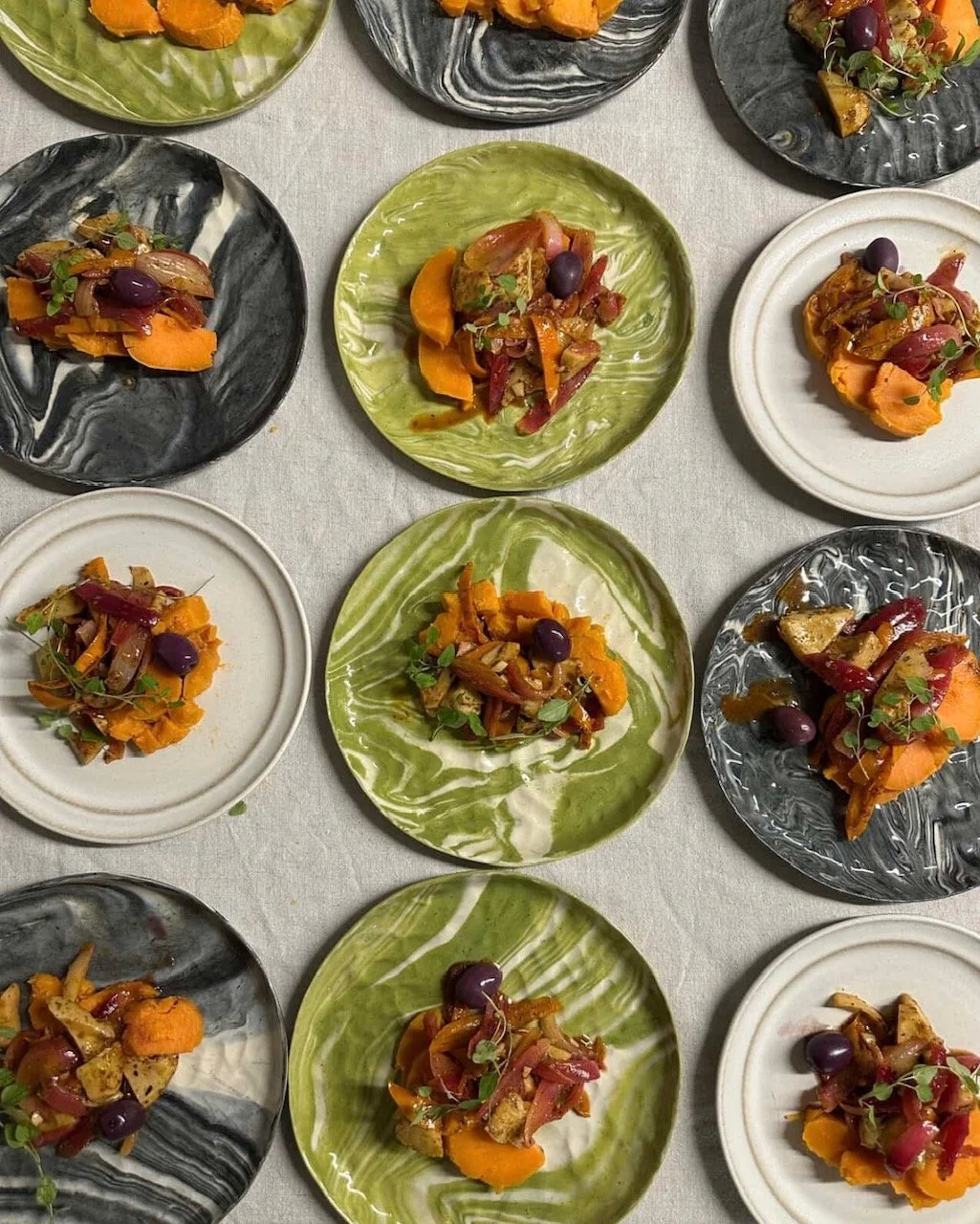 Assorted small plates with roasted vegetables and garnishes on colorful plates, arranged on a table.