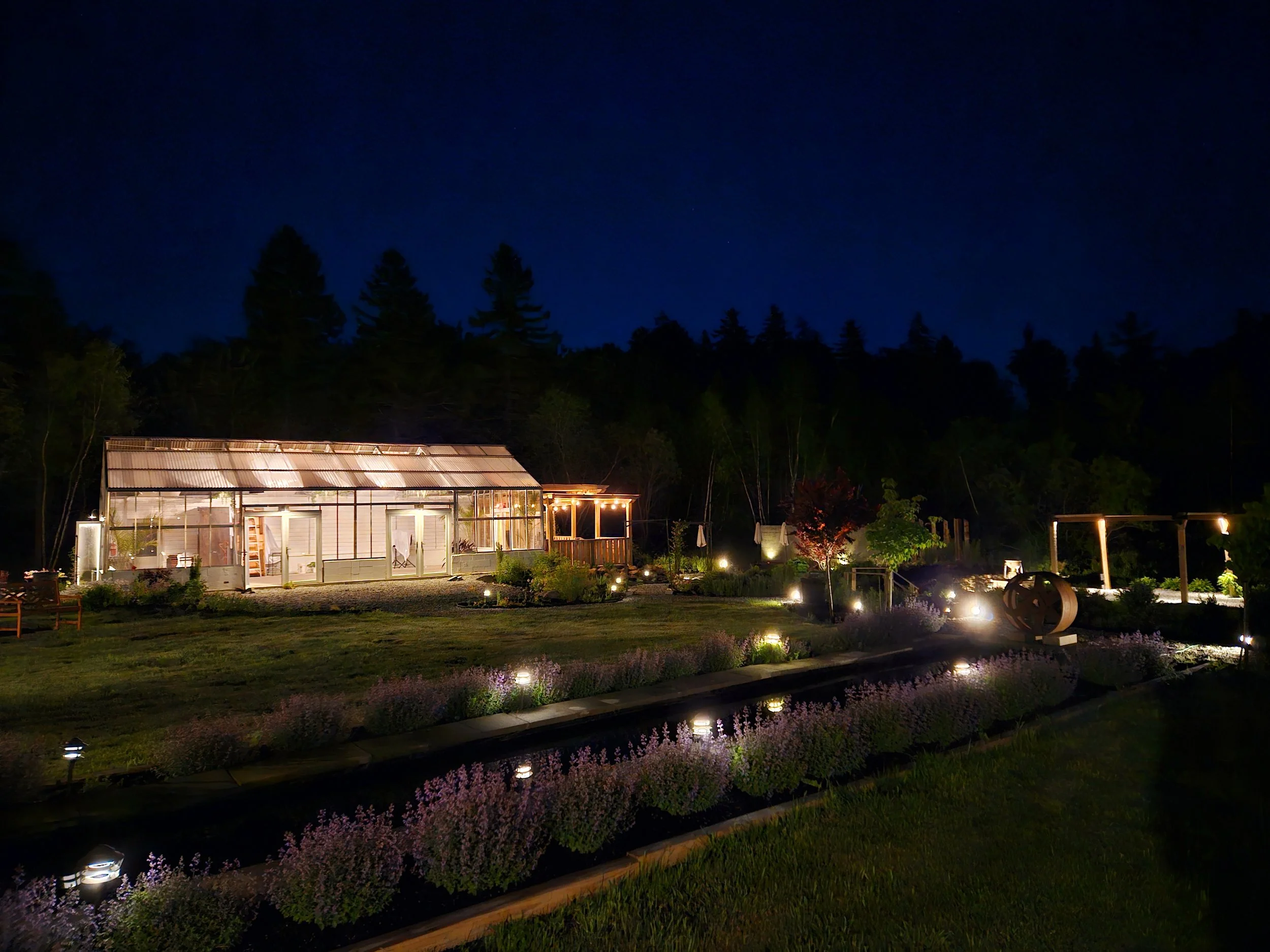 Night view of a garden with a greenhouse, colorful trees, and landscape lighting.