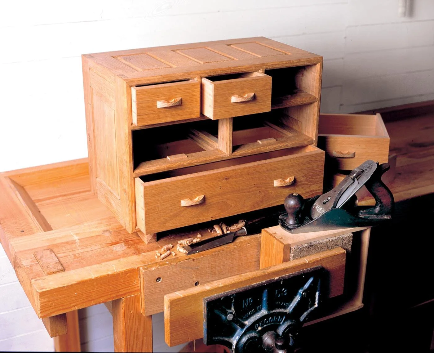 Wooden furniture workshop with a partially assembled small wooden cabinet, woodworking tools and wood shavings on a workbench.