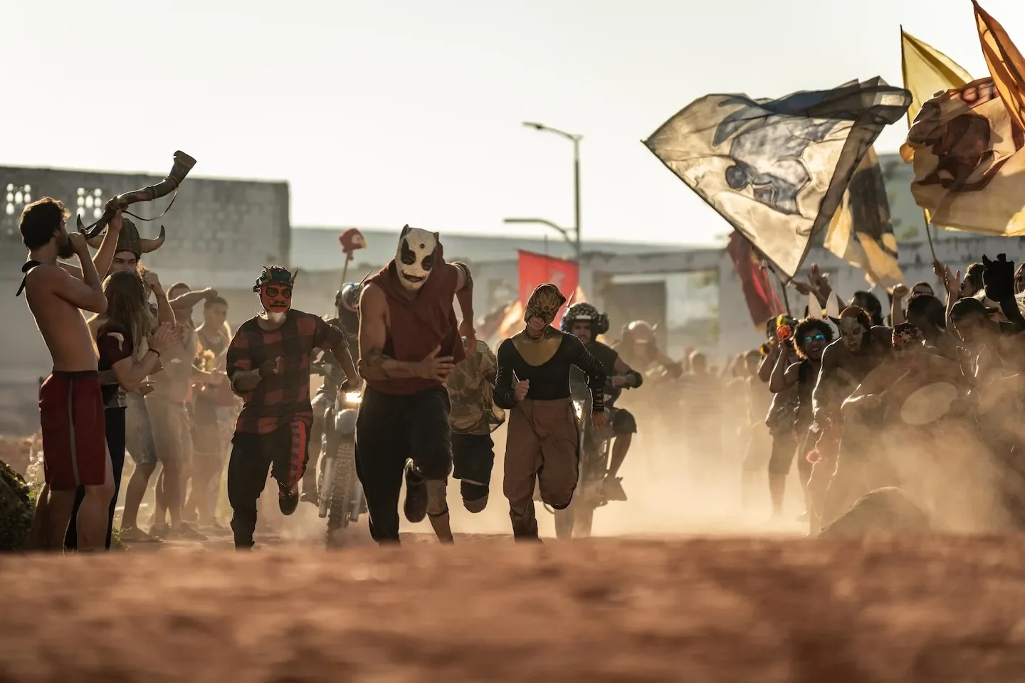People in animal masks run toward the camera through a crowd that is cheering and waving flags