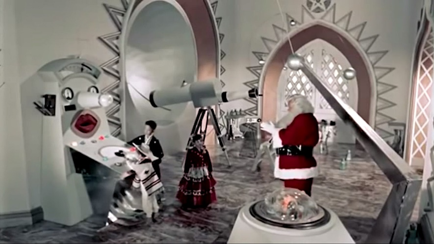 Santa stands in his large, grey, futuristic workshop in front of his telescope