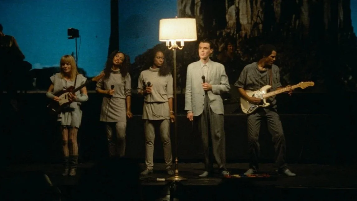Tina Weymouth, Ednah Holt, Lynn Mabry, David Byrne, and Alex Weir stand on stage beside each other in the film, 'Stop Making Sense.'