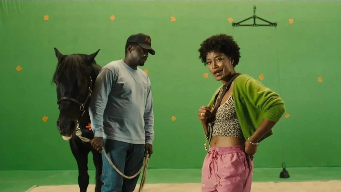 OJ Haywood (played by Daniel Kaluuya) stands in the foreground with his hands on the reins of a horse, as his sister Emerald Haywood (played by Keke Palmer) is front and center in front of a green screen in the film 'Nope.'