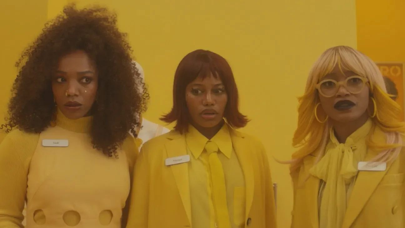 Three Black women, one with curly shoulder length brown hair, one with a red bob, and one with straight blonde hair and glasses, look in different directions with surprised expressions. Their outfits and surroundings are all yellow.