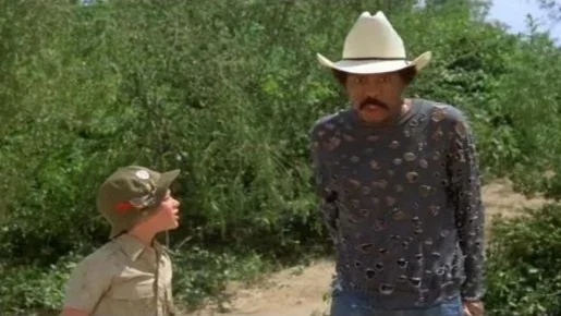 Eric Bates looks towards Jack (Richard Pryor), who has on a hole-ridden shirt, a cowboy hat, and a shocked expression on his face.