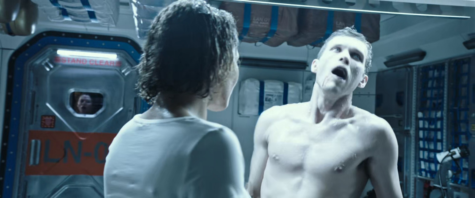 A woman with her back to the camera stands in front of a pale, shirtless man who looks possessed - mouth agape, pale, and sweaty