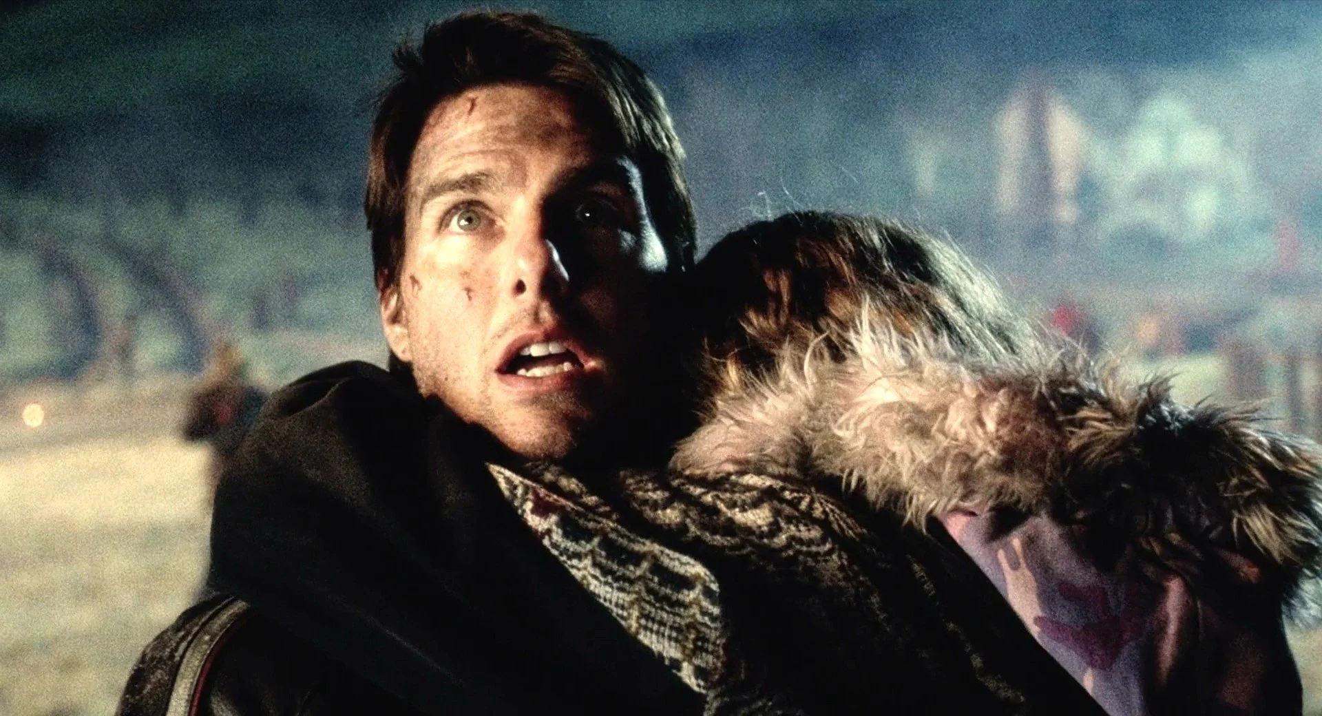 Tom Cruise, holding a child to his chest, looking above the camera with an awed expression on his face.