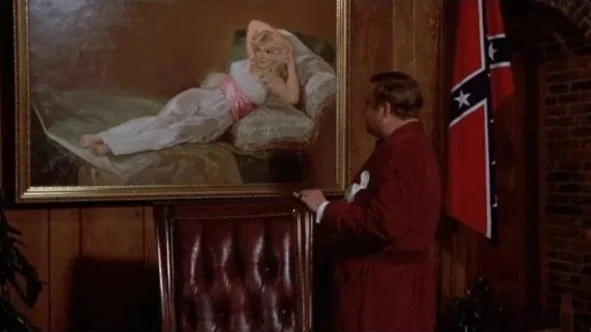 cU.S. Bates (played by Jackie Gleason) looks at a painting of his wife, as a Confederate flag stands beside him.