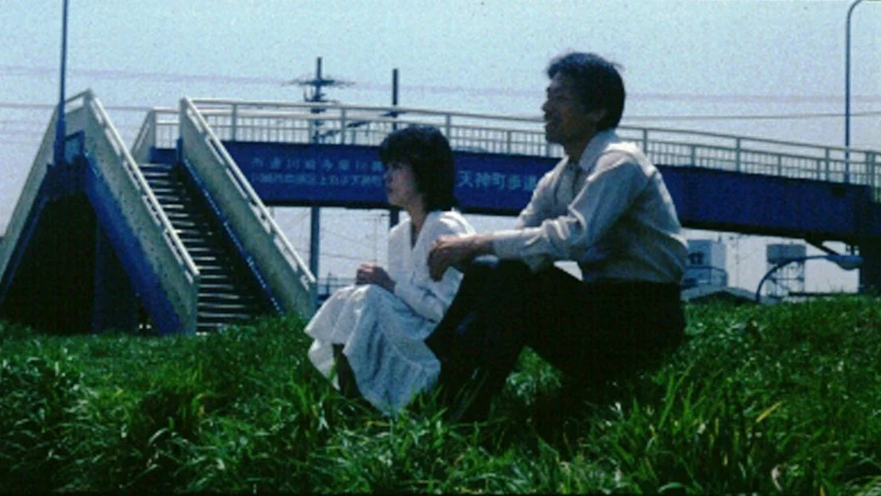 Kaoru Kaze as the young bride, Yoriko, sits in a grassy field next to her husband Koichi, played by Shirô Shimomoto in the film, Abnormal Family.