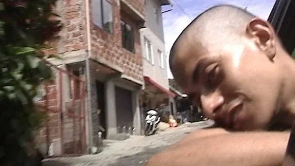 An unnamed youth character leans his head out the window of a car driving through the streets in the film Barrio Triste.