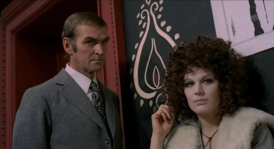 Inspector Corvin (Stanley Baker) looks off-screen in the same direction as Jenny (Penny Brown) in the film A Lizard In a Woman's Skin.