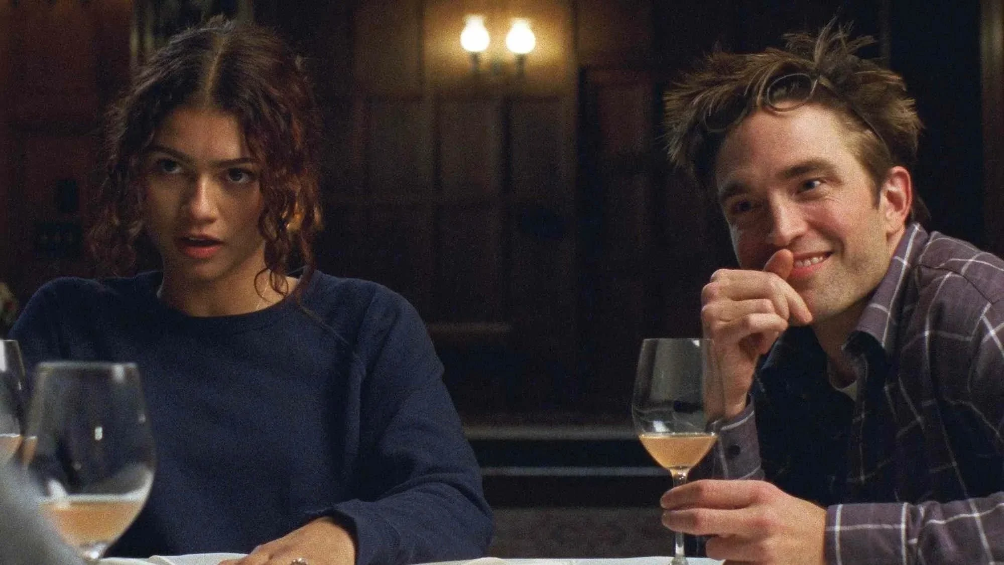 Emma (Zendaya) looks gobsmacked as she sits next to her fiance, Charlie (played by Robert Pattinson), who is hiding a smirk behind his hand in the film, 'The Drama.'